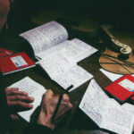 Many red notebooks lie partially open on a desk while someone is writing in one of them.