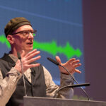 Martin Schleske spricht in zwei Mikrofone an einem Rednerpult.