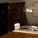 Arbeitstisch mit Lampe und Stuhl und im Hintergrund Werkzeuge